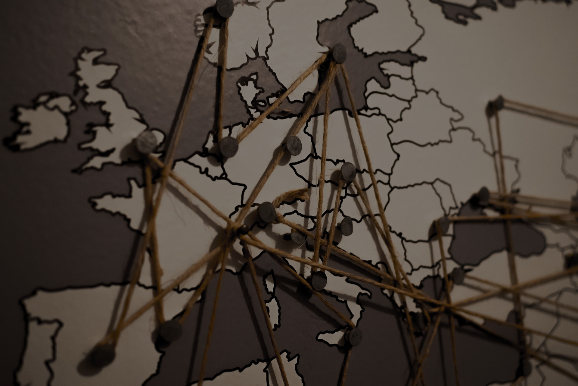 A close-up of a map of the world in greyscale, with points connected by a thread